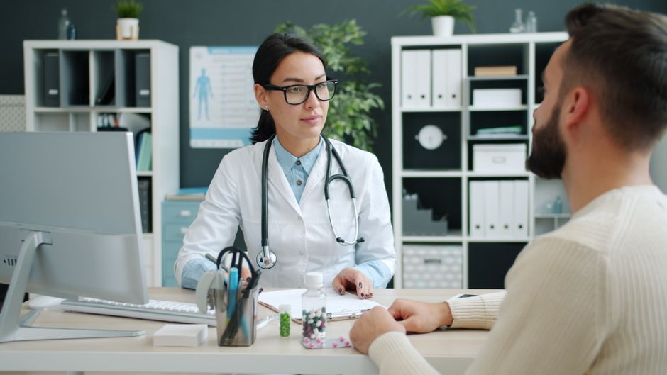 Medical professional writing patient notes on clipboard during consultation.