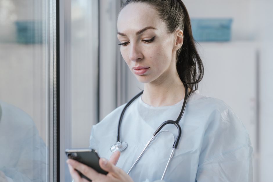 Portrait of a female doctor in a disposable gown using a smartphone in a hospital environment.