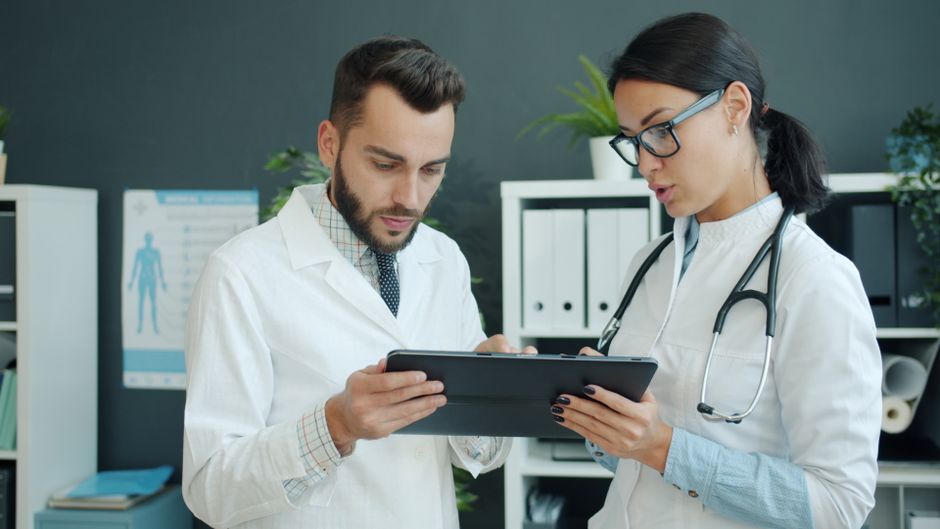Two doctors reviewing medical information on a tablet in a clinical setting.